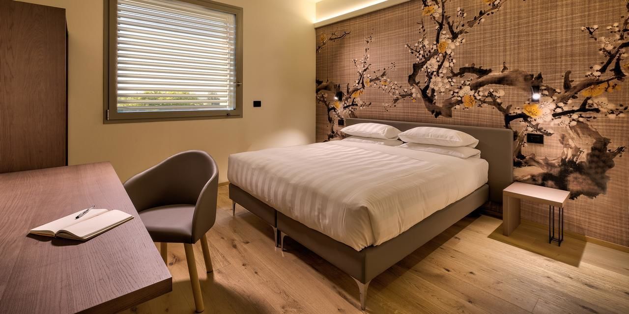 A bedroom with a bed, bedside table, chair, and a desk with a book.