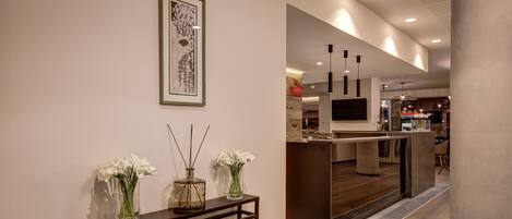 A modern interior with a console table, vases with white flowers, a framed artwork, and a kitchen area in the background.