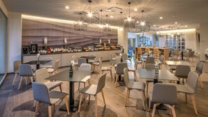 Un comedor moderno con mesas y sillas, una zona de bar con mostrador, y vistas de la ciudad a través de grandes ventanales.