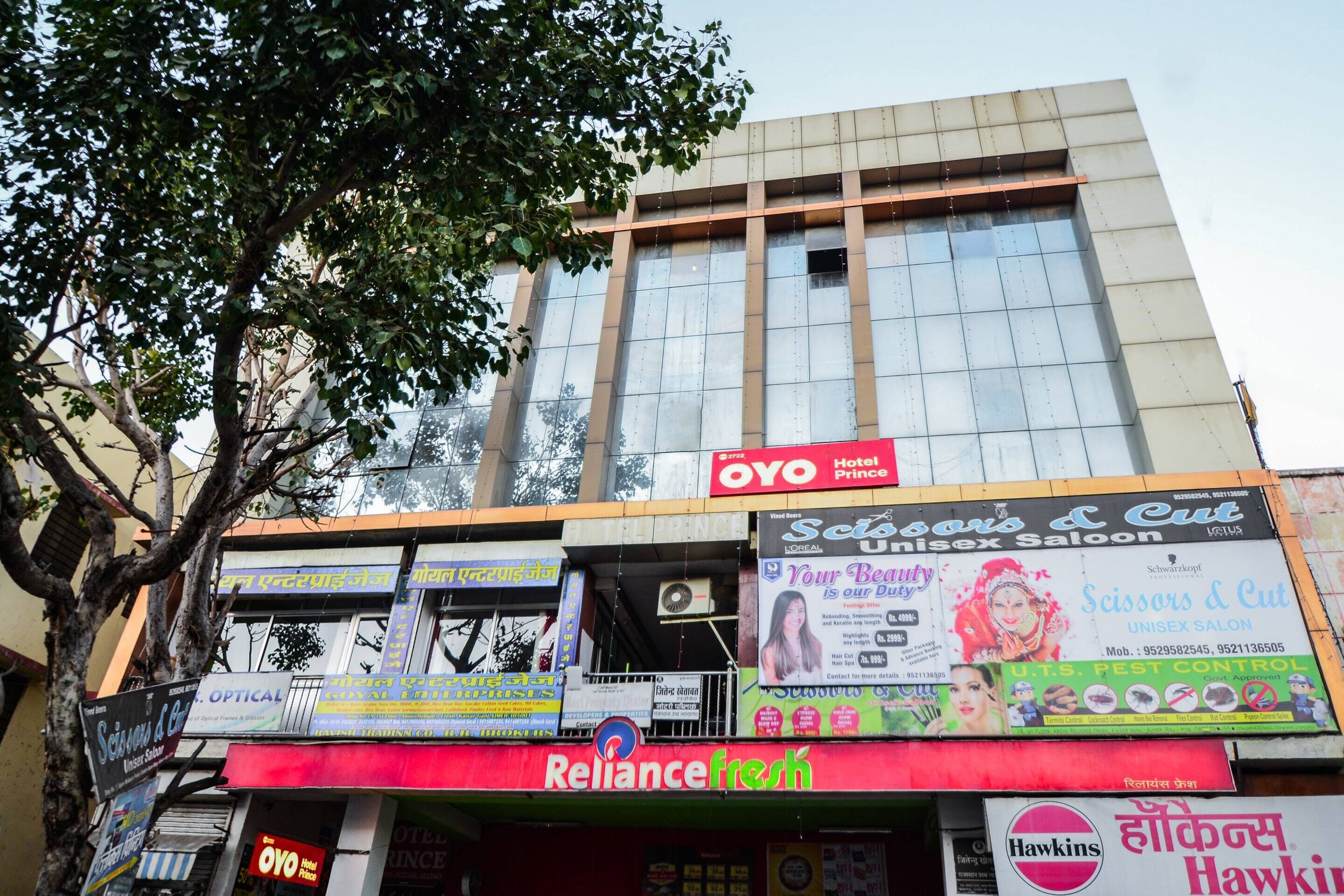 A building with multiple commercial establishments including a hotel named OYO Hotel Prince, a salon, and a pest control service.