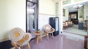 A lobby with wicker chairs, a small round table, and a refrigerator. - RedDoorz Plus near STIE YKPN (Depok)
