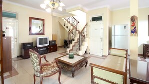 A living room with a wooden coffee table, two chairs, a television, a staircase, and a refrigerator. - RedDoorz Plus near STIE YKPN (Depok)
