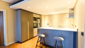 Una cocina moderna con una isla central, taburetes de bar, electrodomésticos integrados y piso de madera.