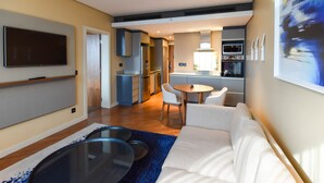 Una sala de estar moderna con un sofá, una mesa de centro y un televisor. Cuenta con una zona de cocina con una mesa de comedor y sillas.