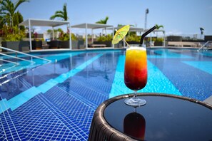 A poolside setting with a drink on a table and a pool in the background. - Hotel 2 Février Lomé Appartement (Lomé)