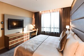 A hotel room with a large bed, a flat-screen TV mounted on the wall, a desk with a chair, and a window with curtains. - Hotel 2 Février Lomé Appartement (Lomé)