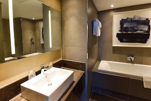 A modern bathroom with a large mirror, a white sink, and a bathtub. - Hotel 2 Février Lomé Appartement (Lomé)