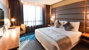 Una habitación de hotel con una cama grande, un escritorio, una silla, un televisor y una ventana con cortinas.