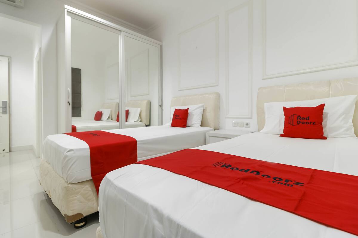 A hotel room with two beds, each with a red bedspread and pillows, and a large mirror on one wall.