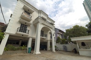 A multi-story building with a central archway, balconies, and a parking area.