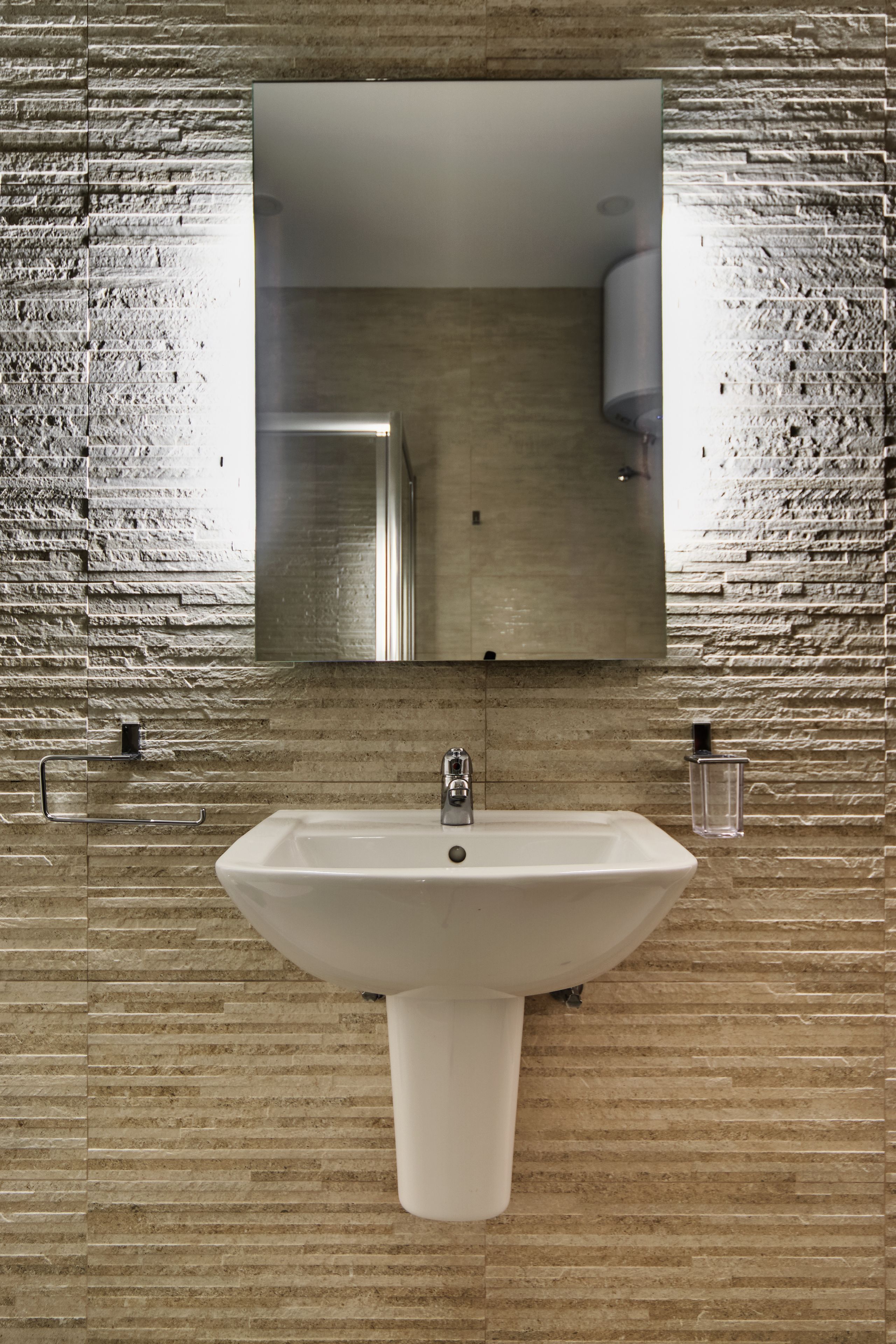A bathroom with a rectangular mirror above a pedestal sink, set against a textured stone wall.