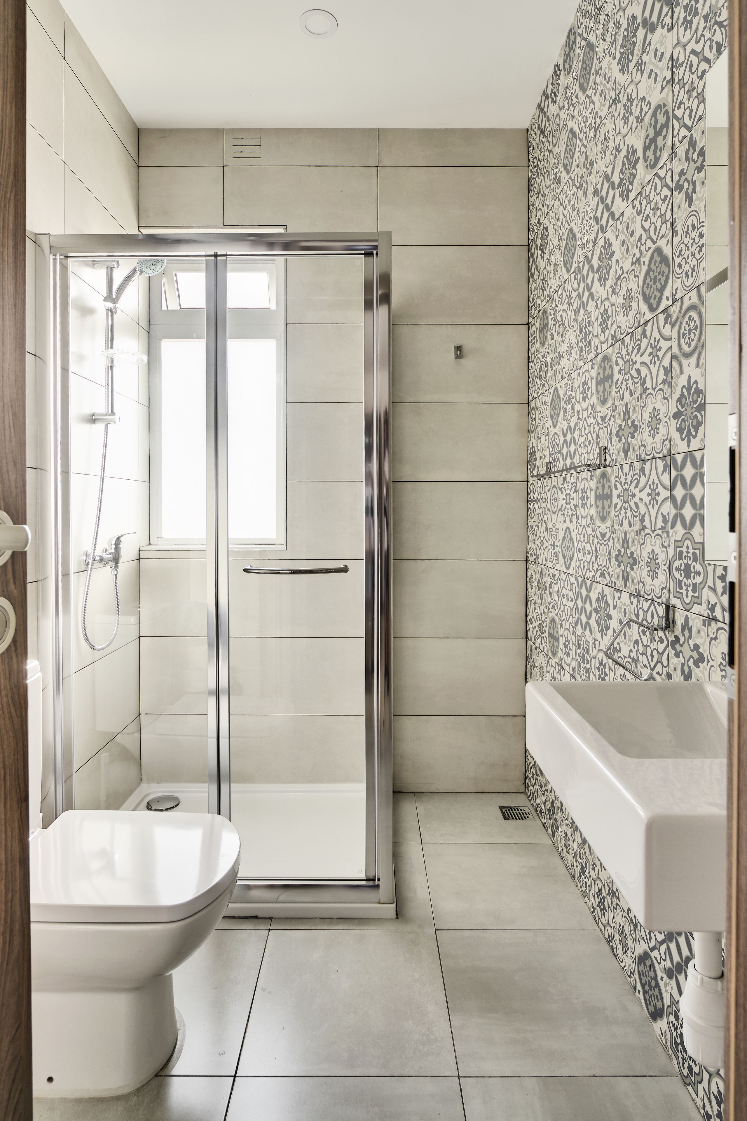 A modern bathroom with a glass-enclosed shower, a white toilet, and a patterned tile backsplash.