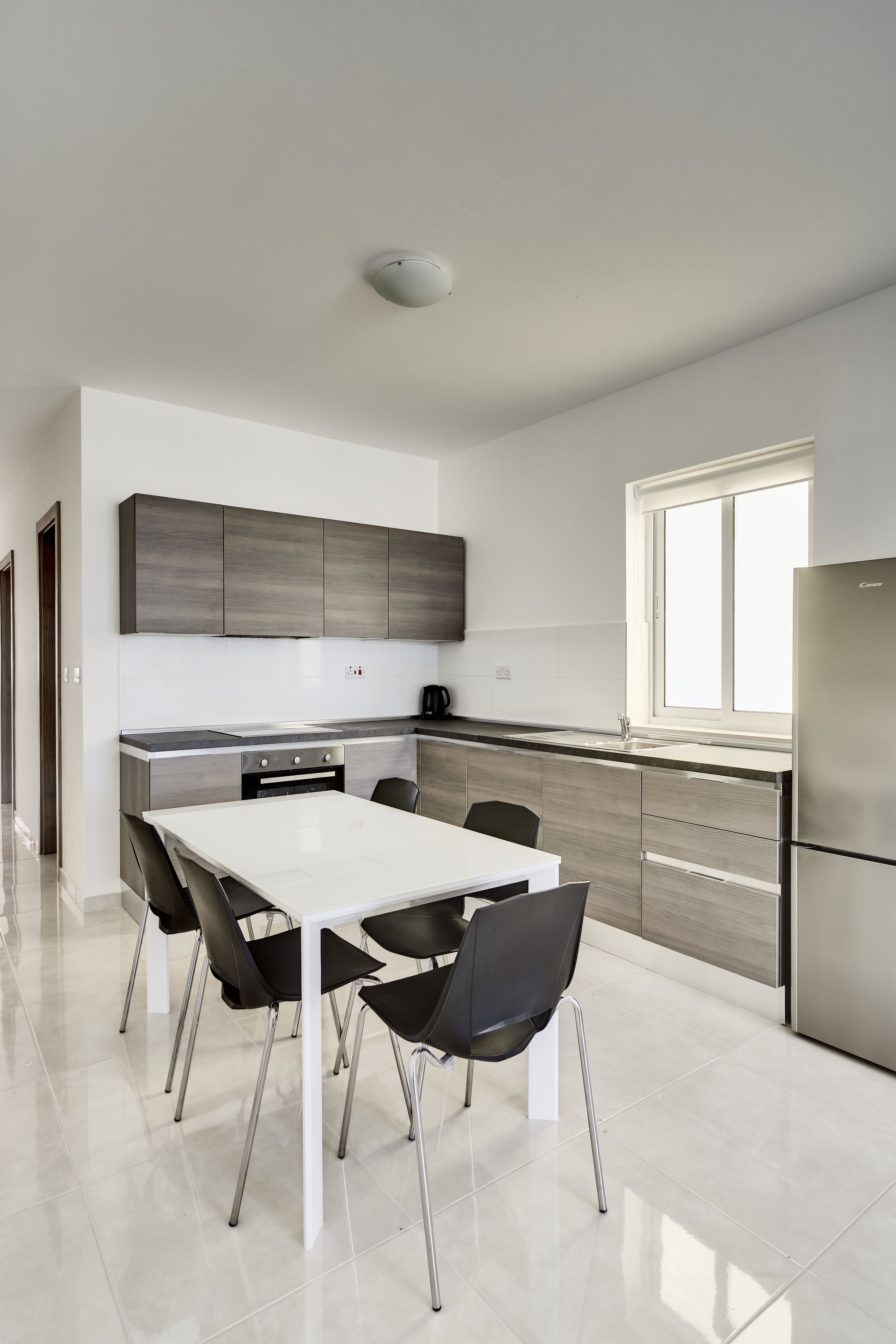 Une cuisine moderne avec une table et des chaises blanches, des appareils électroménagers en acier inoxydable et une fenêtre laissant entrer la lumière naturelle.