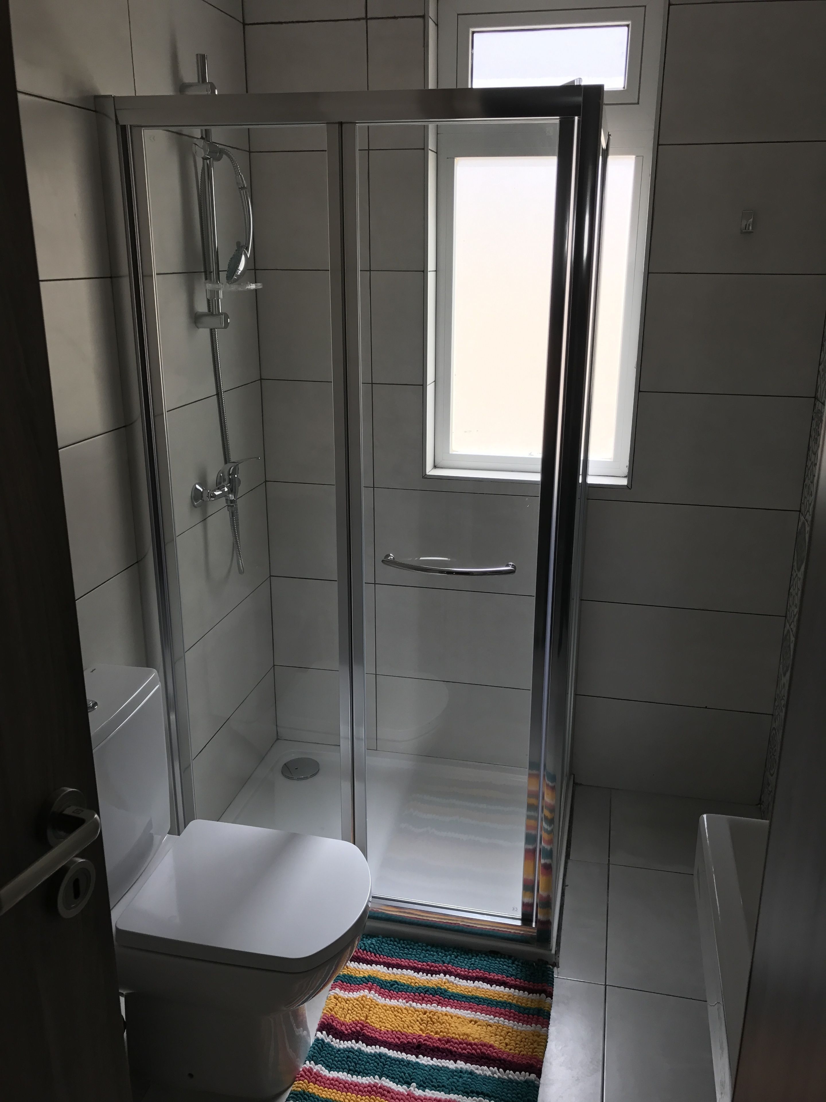Une salle de bain moderne dotée d’une douche à parois de verre, de toilettes et d’une fenêtre laissant entrer la lumière naturelle.