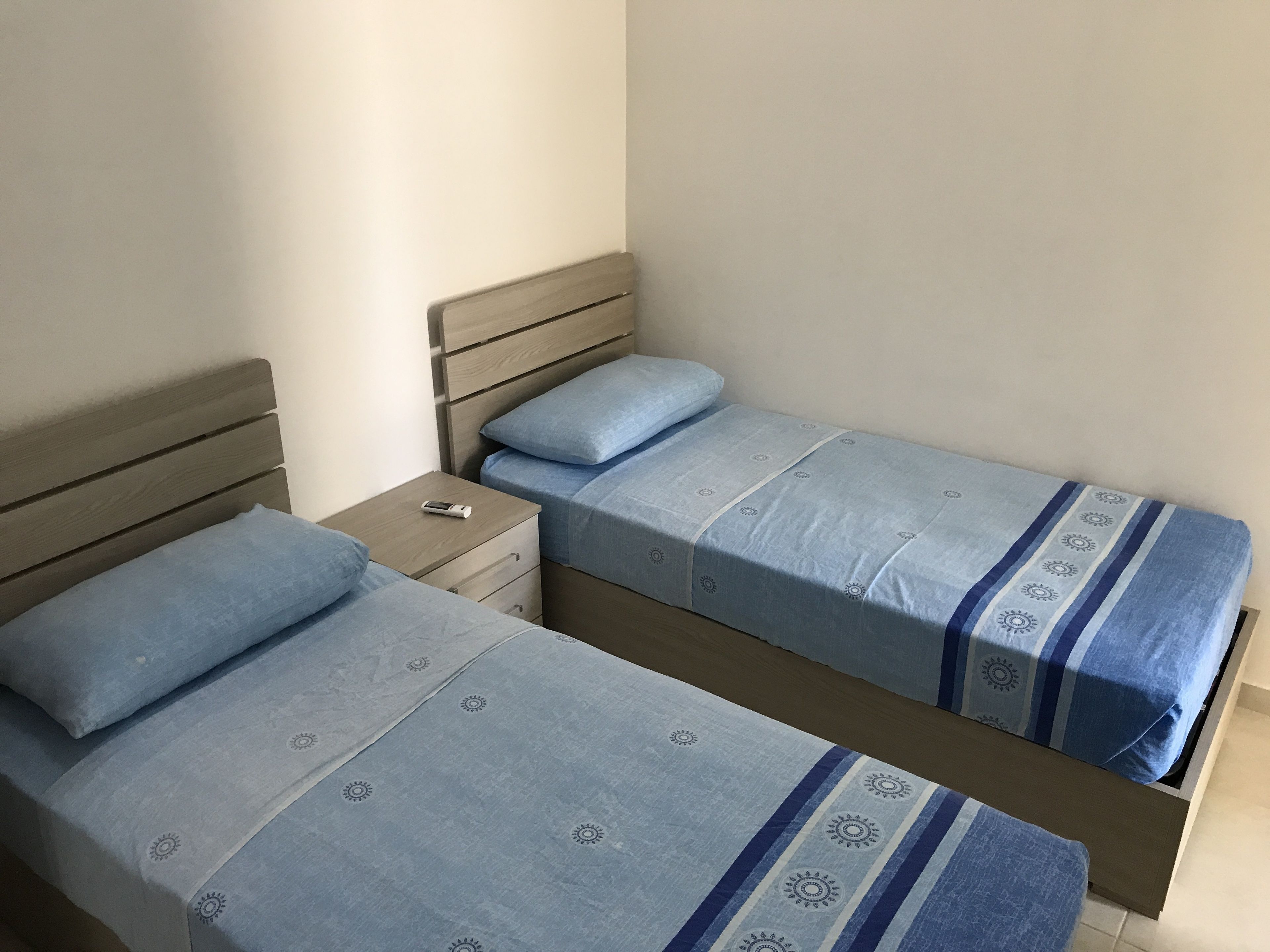 A bedroom with two single beds, each with a wooden headboard and a blue bedspread with a sun pattern.