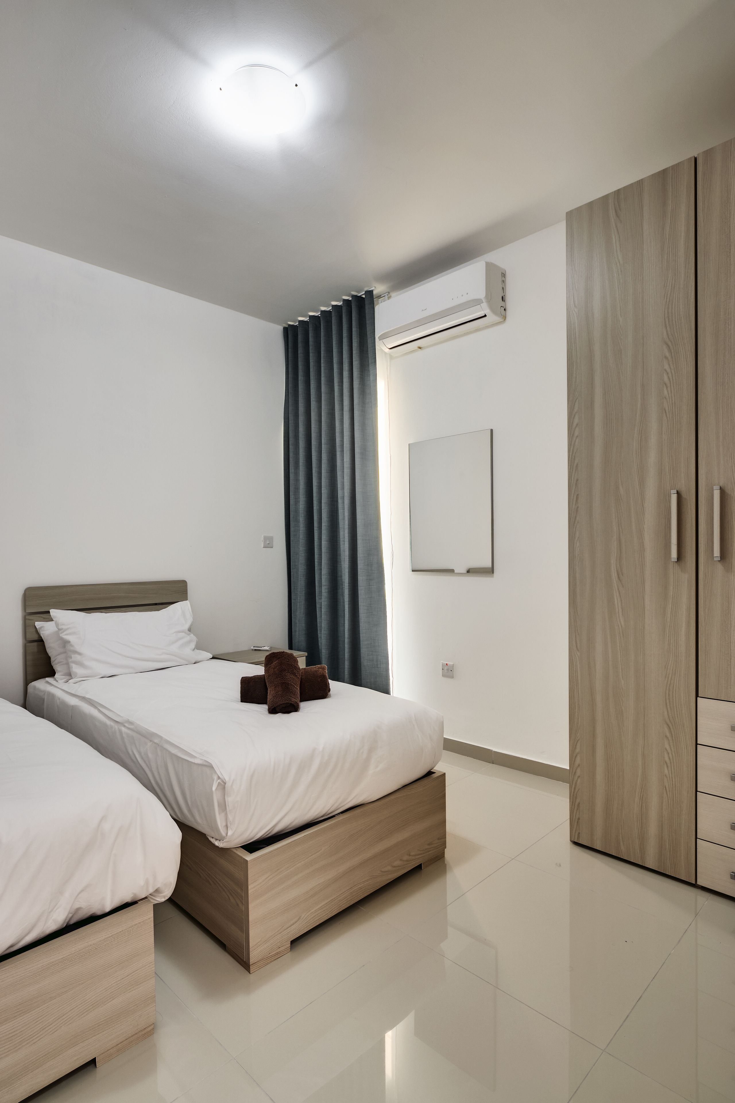 Una habitación de hotel moderna con dos camas, un armario y una lámpara de techo.