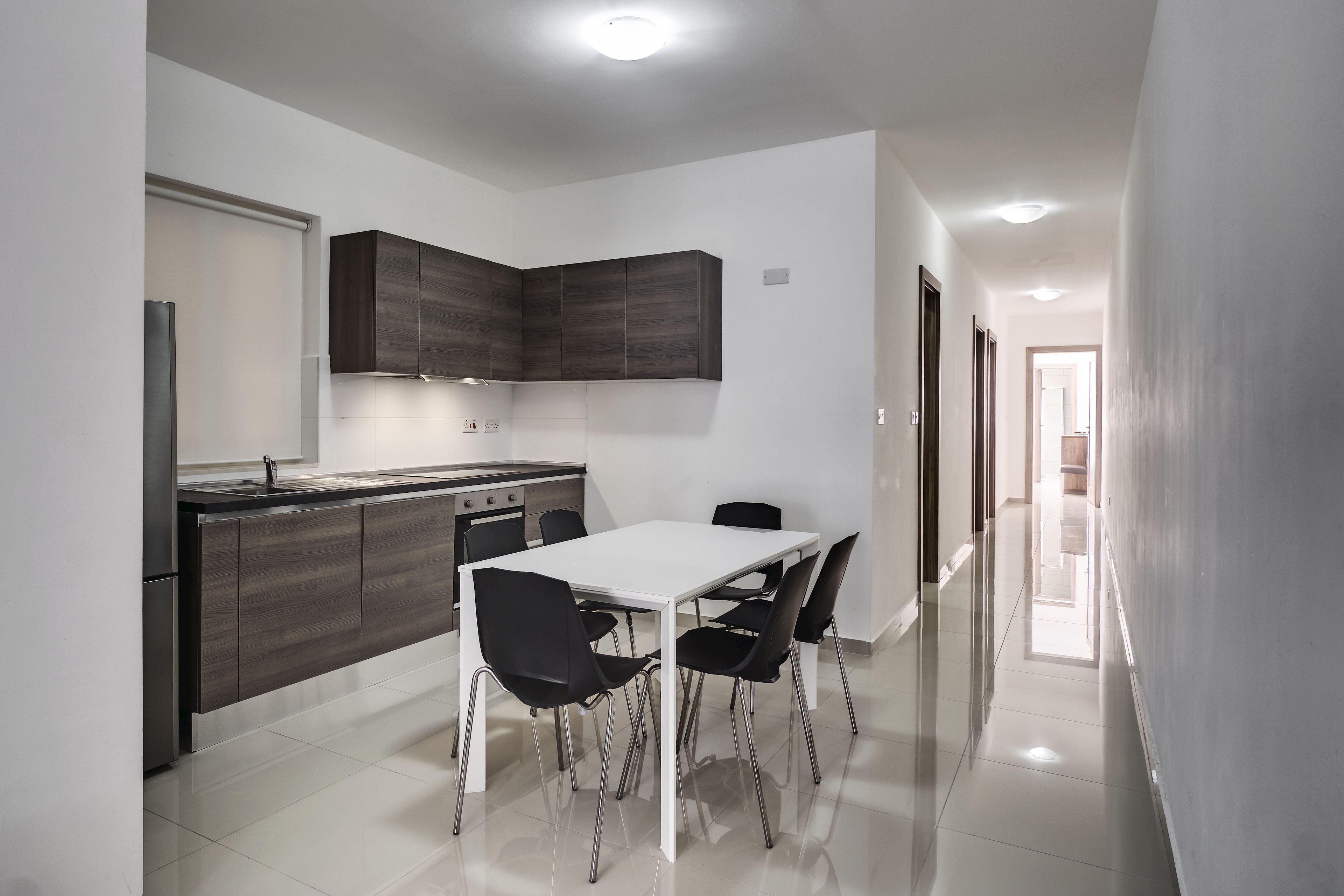 A modern kitchen with a white table and black chairs, a built-in oven, and dark cabinetry.