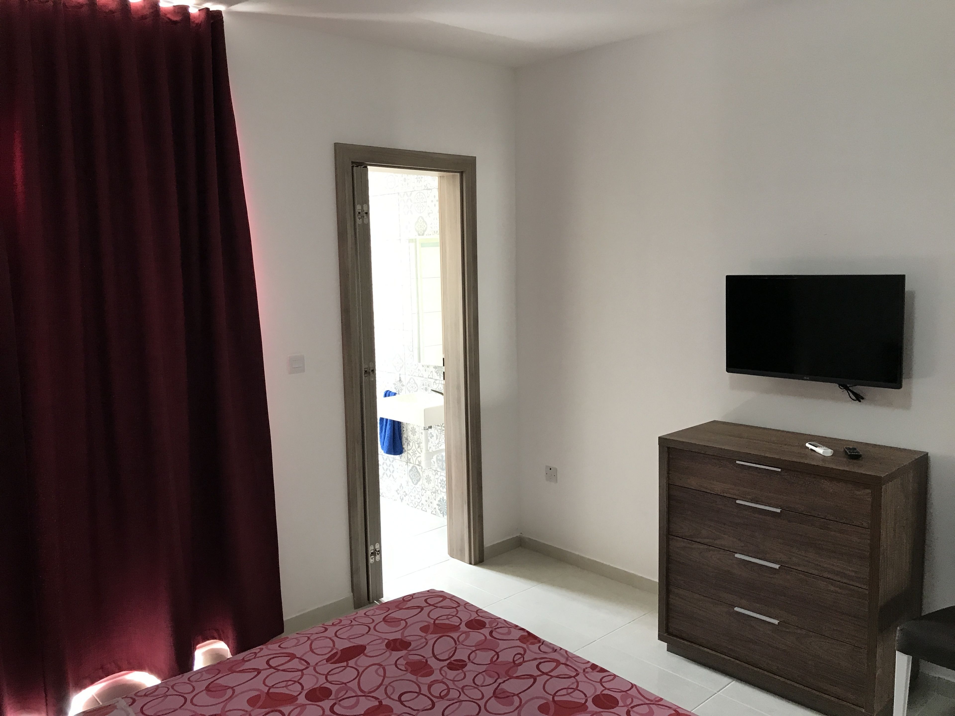 A bedroom with a bed, a dresser, a television, and a door leading to a balcony.