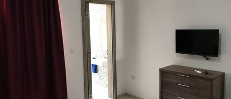 A bedroom with a bed, a dresser, a television, and a door leading to a balcony.