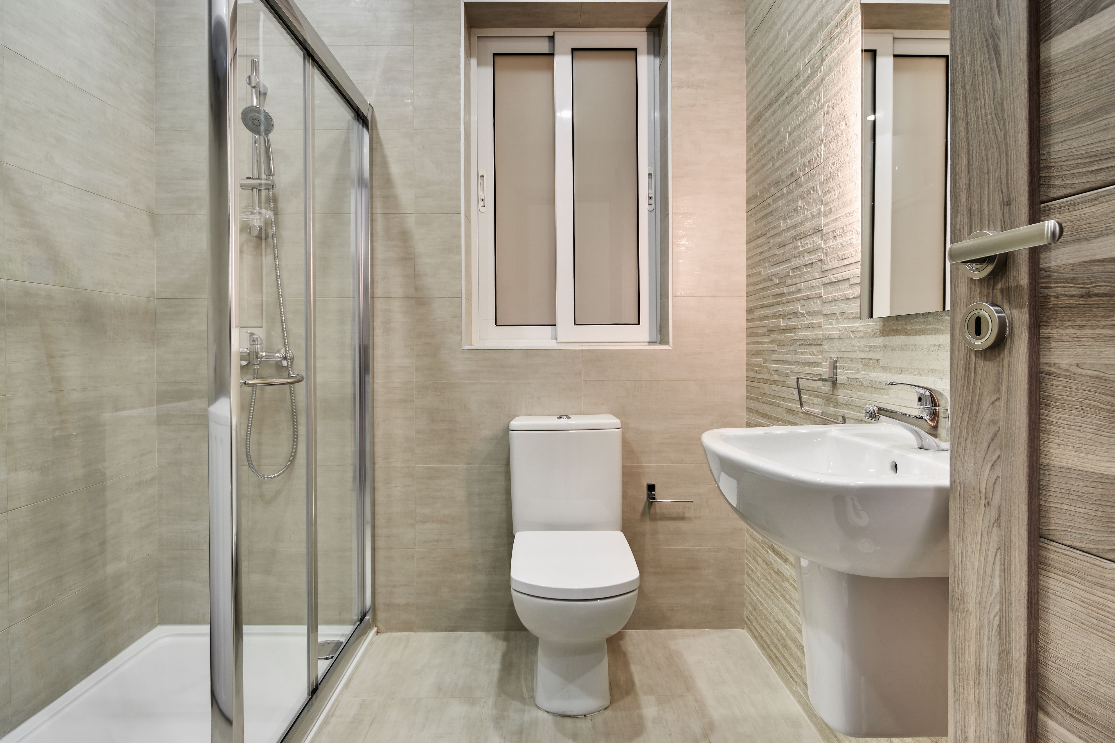 A modern bathroom with a glass-enclosed shower, a toilet, and a sink.