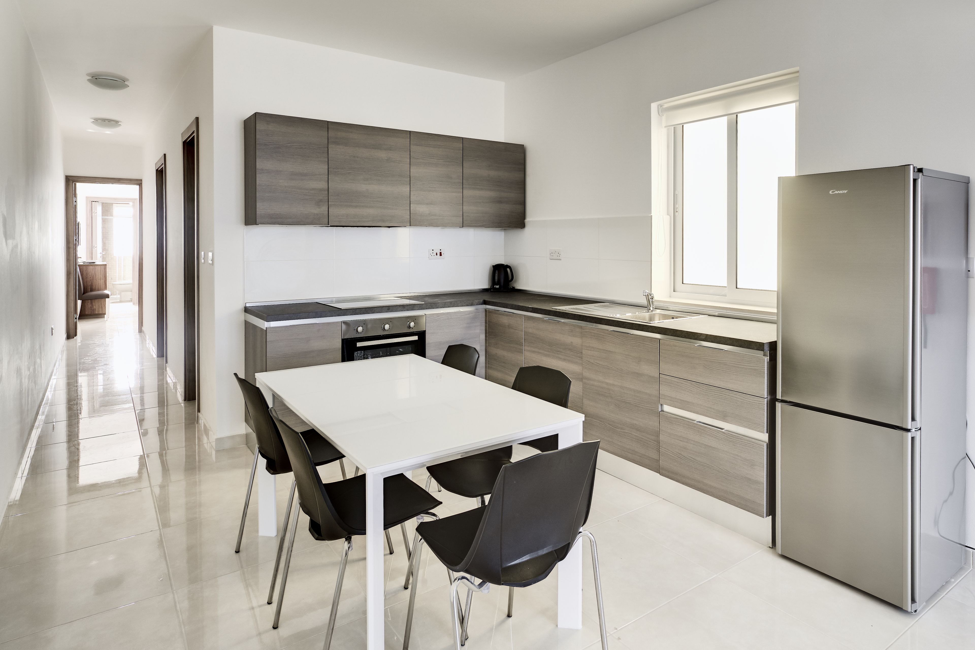 A modern kitchen with a white dining table, black chairs, stainless steel appliances, and wooden cabinets.
