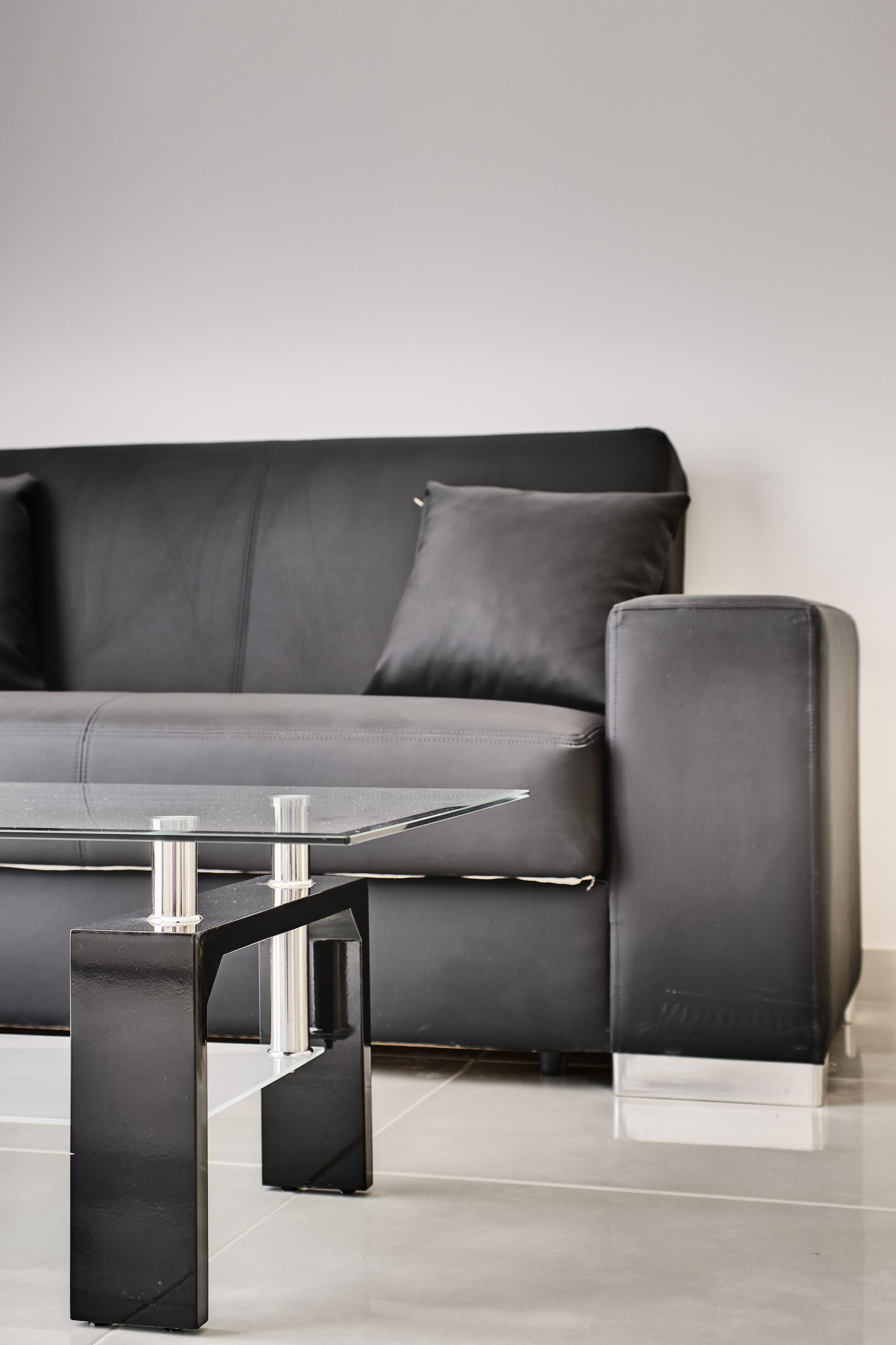Ein modernes Wohnzimmer mit einem schwarzen Ledersofa, einem Glastisch mit Metallbeinen und einem passenden Hocker.