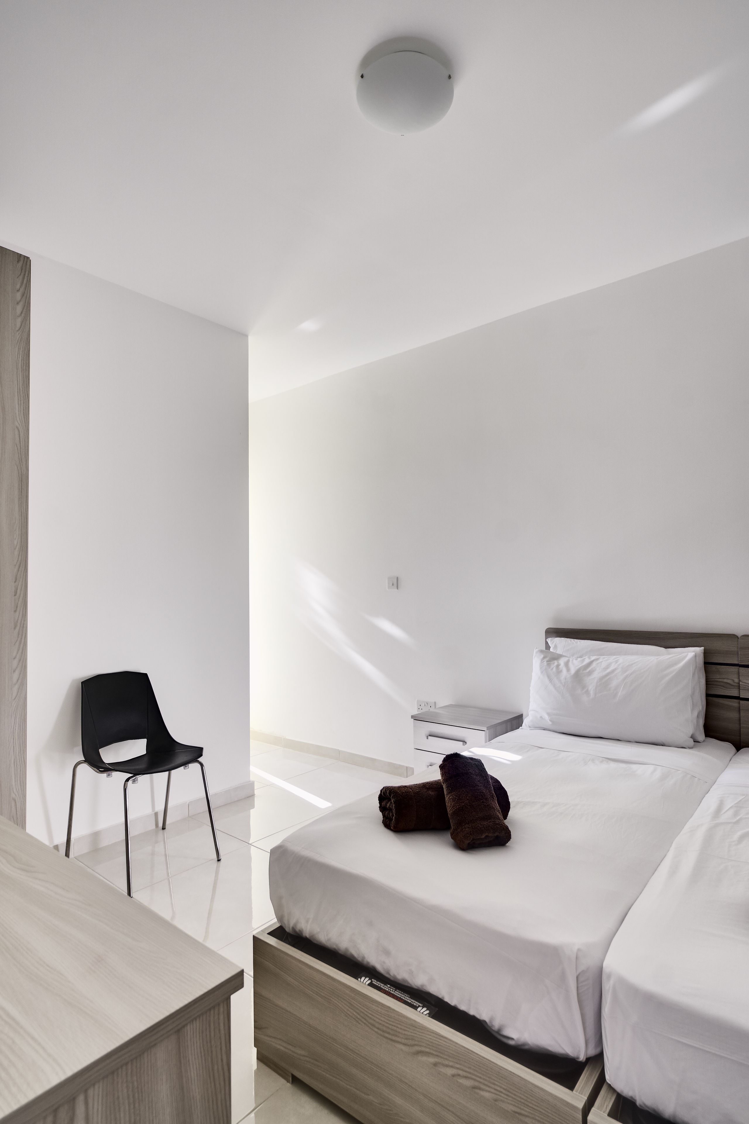 Ein modernes Hotelzimmer mit einem Holzbüro, einem schwarzen Stuhl, einem Bett mit weißer Bettwäsche und einem Nachttisch.