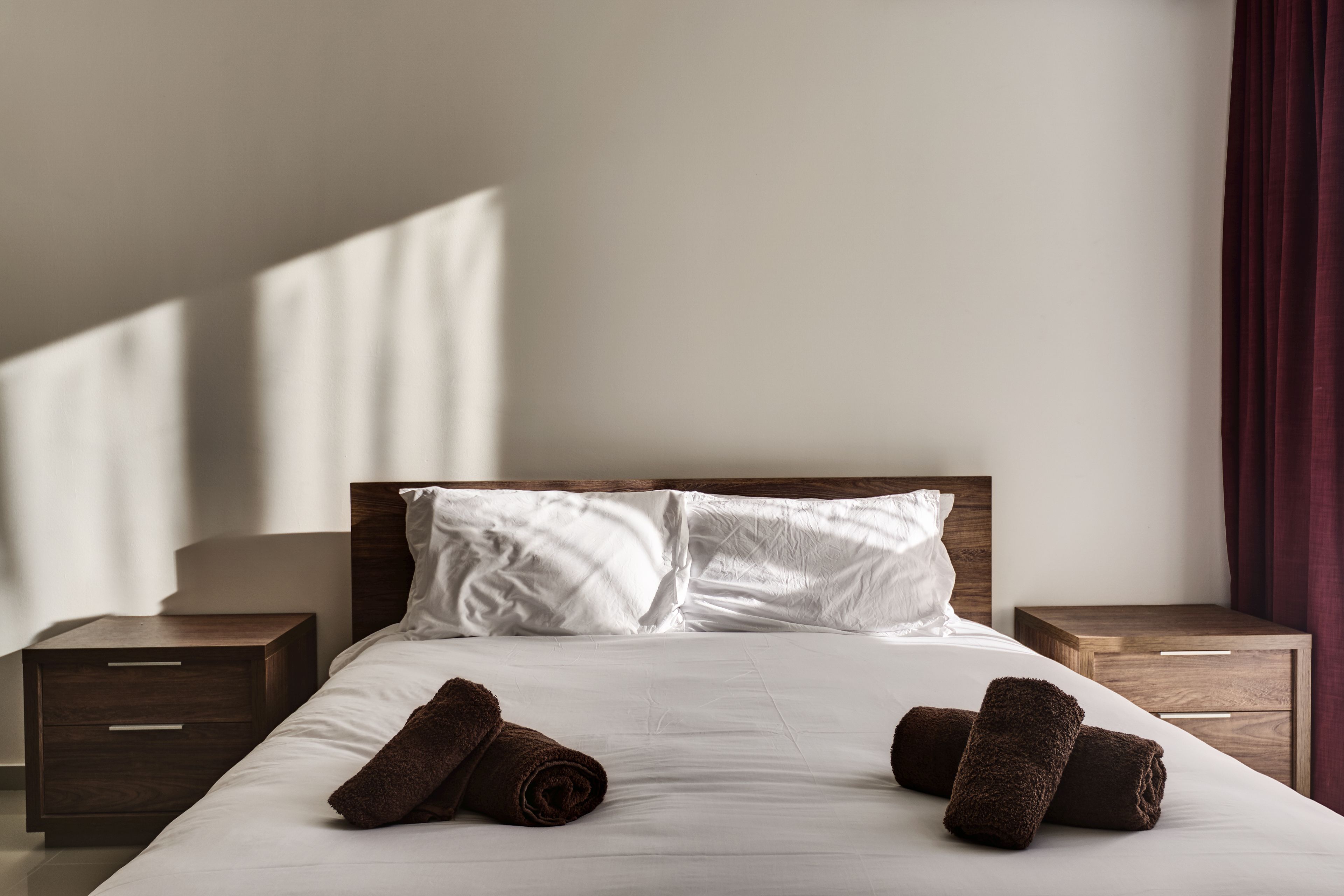 A neatly made bed with white linens and two brown towels, wooden headboard, and nightstands with drawers.