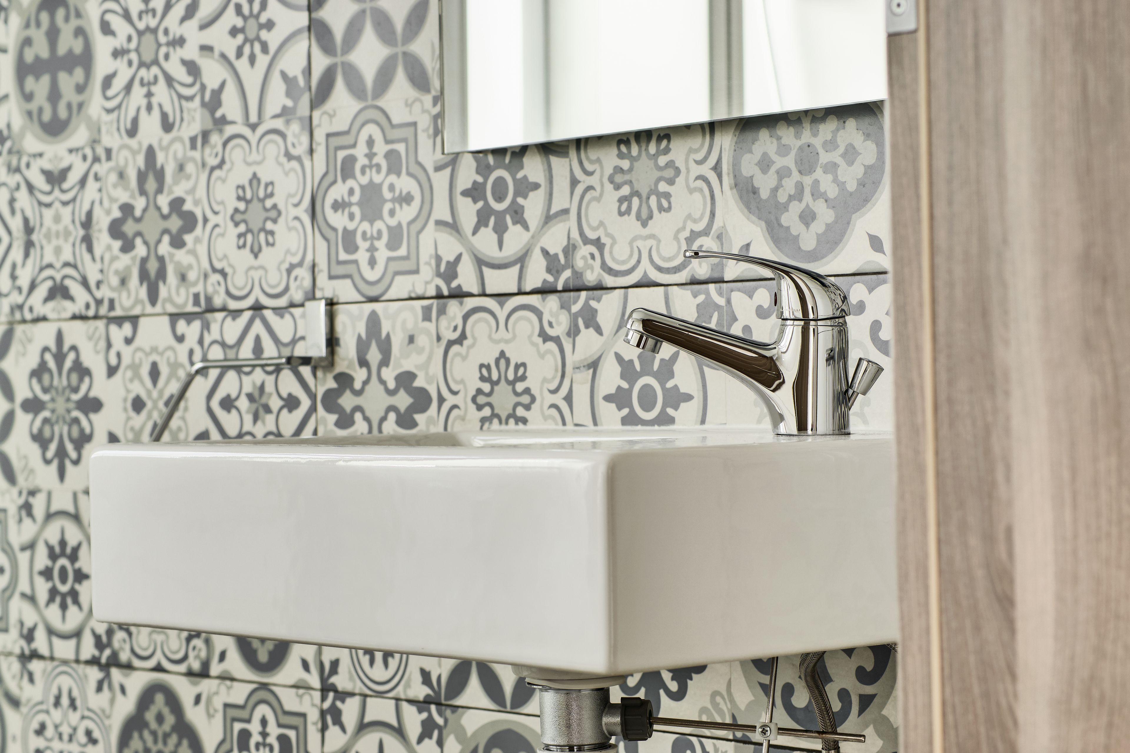 Un bagno con lavandino bianco, rubinetto cromato e schienale piastrellato decorativo.