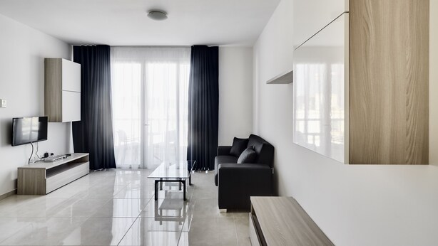 A modern living room with a flat-screen TV, a sofa, a coffee table, and a wooden cabinet. - The Village Apartments (St. Paul's Bay)
