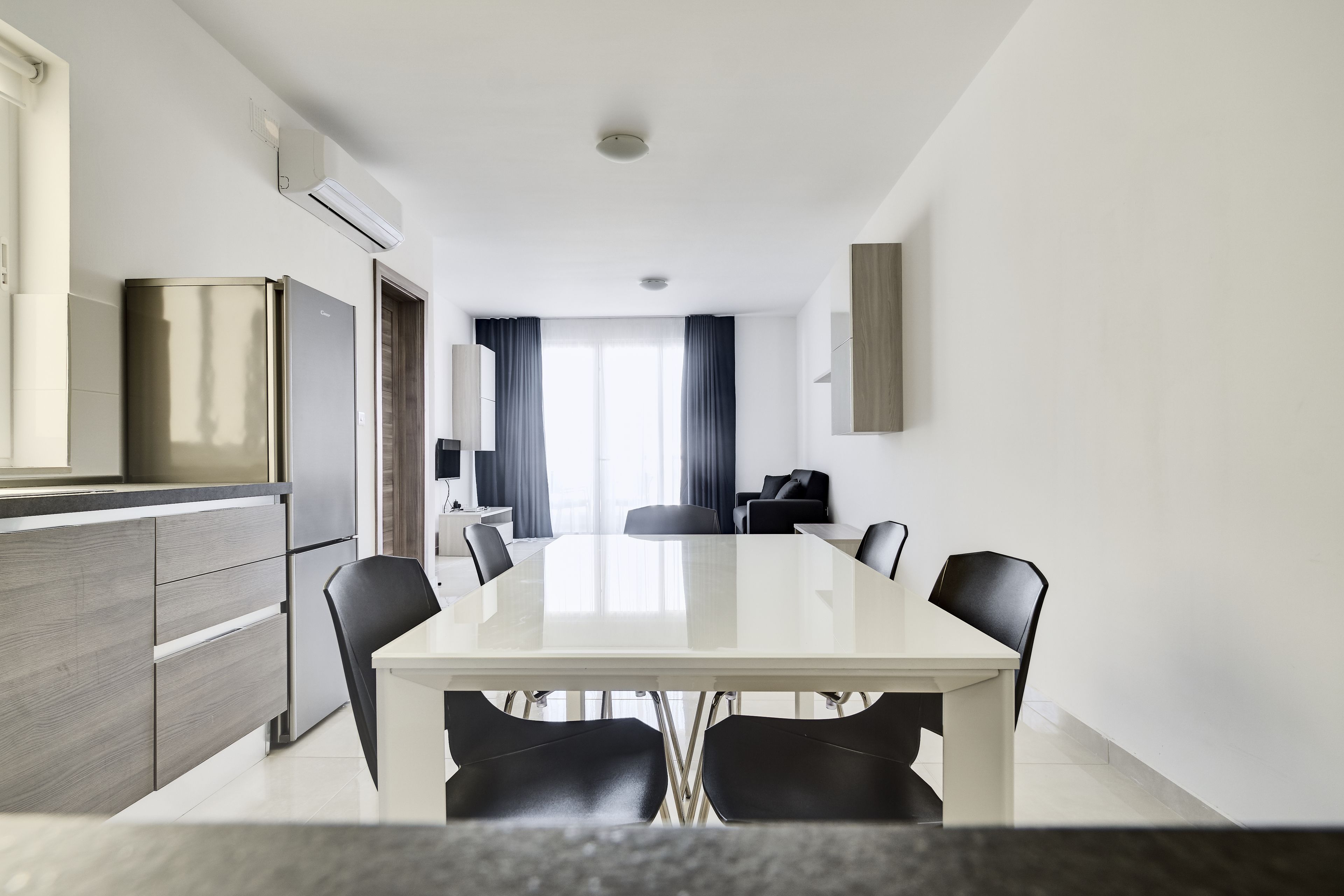 Una moderna camera d'albergo con zona pranzo che include un tavolo e sedie, angolo cottura con frigorifero, e salottino con divano e poltrone.