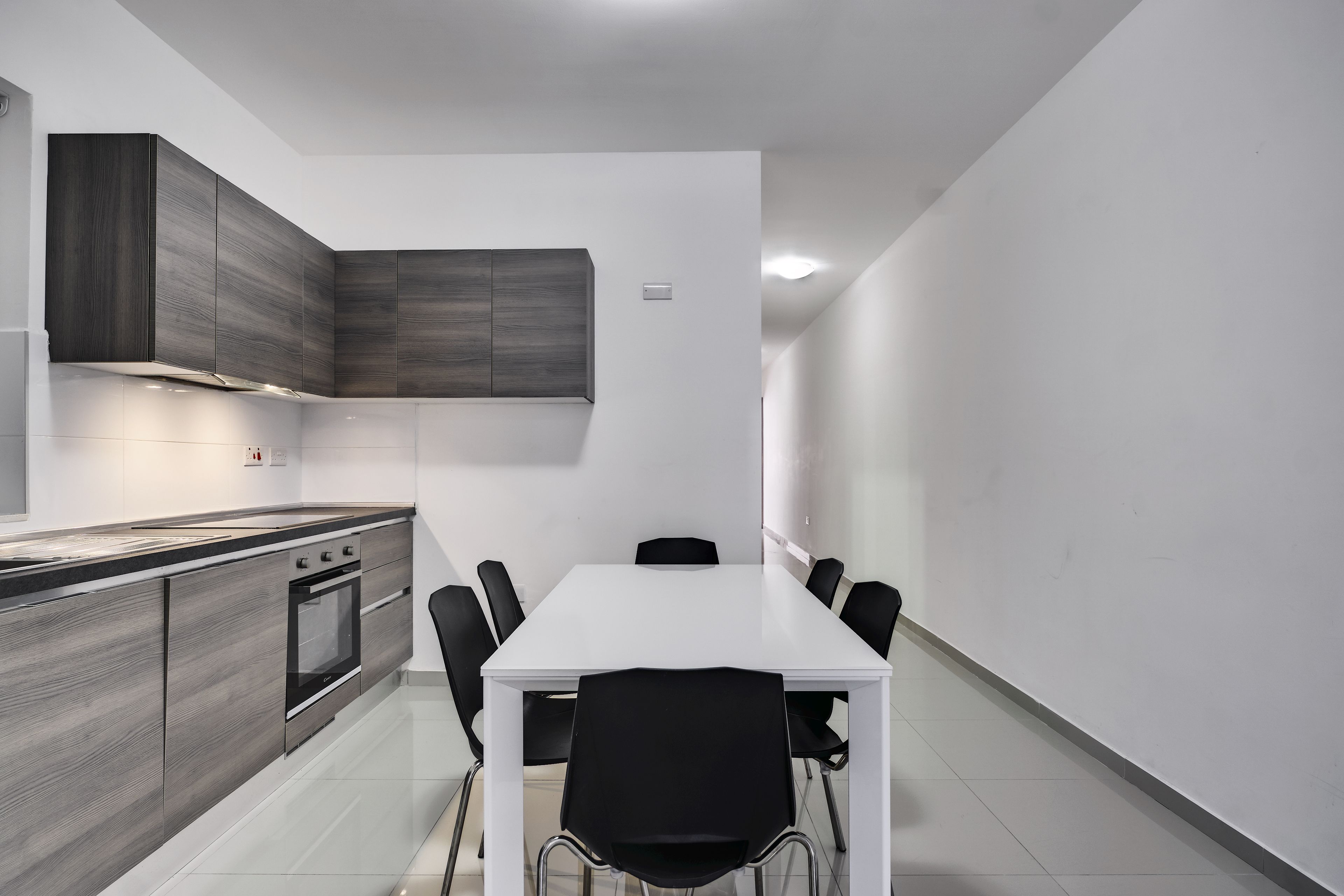 A modern kitchen with a white table and black chairs, a built-in oven, and grey cabinetry.