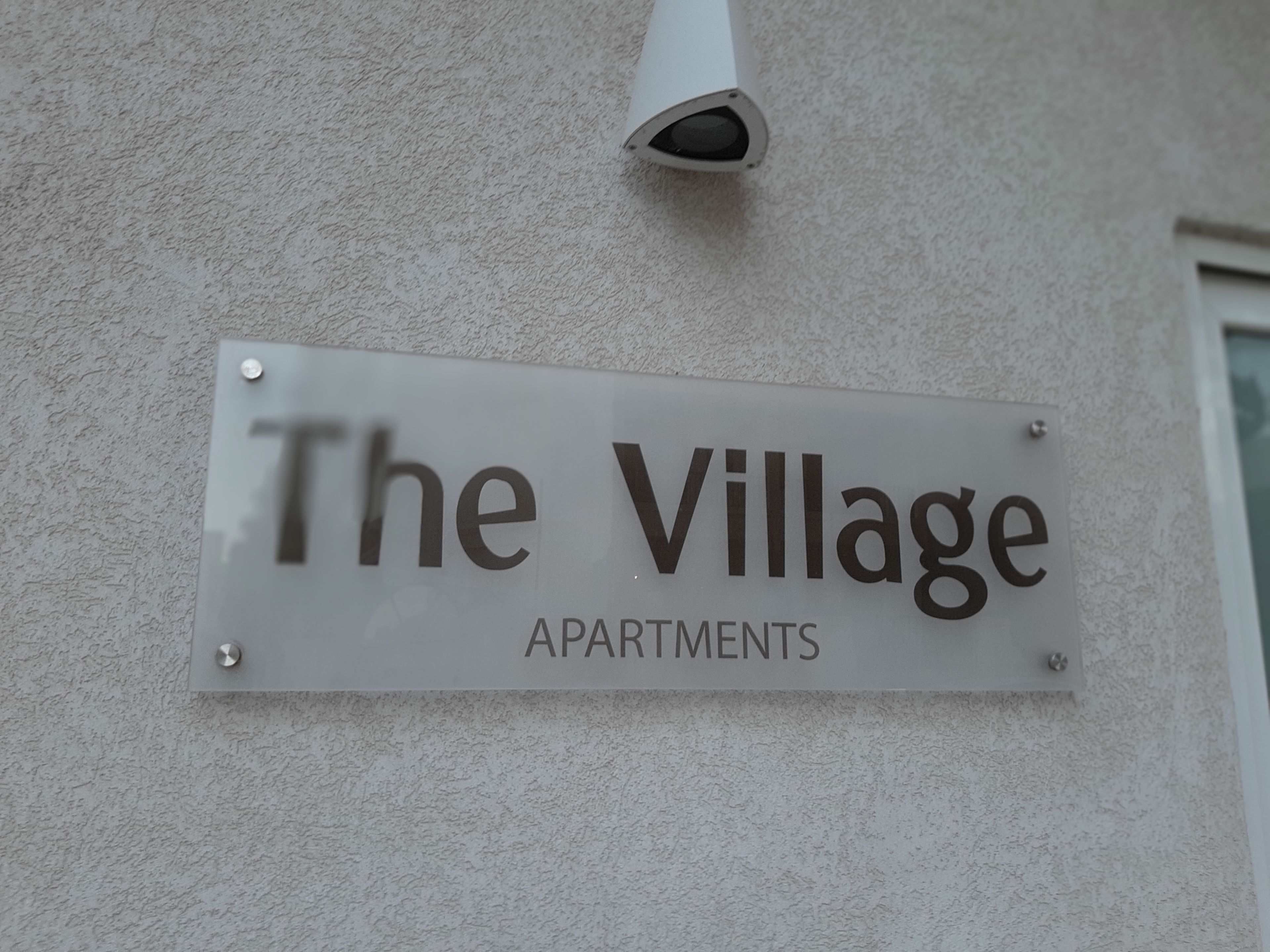 A sign for "The Village Apartments" mounted on a textured wall.