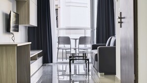 A modern living room with a sofa, two chairs, a small table, and a TV mounted on the wall. - The Village Apartments (St. Paul's Bay)