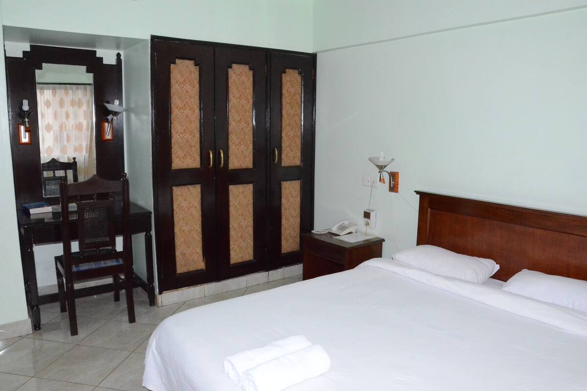 A hotel room with a bed, a desk, a wardrobe, and a mirror.