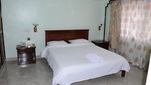 Una cama bien hecha con sábanas blancas, cabecera de madera, mesita de noche con lámpara y teléfono.