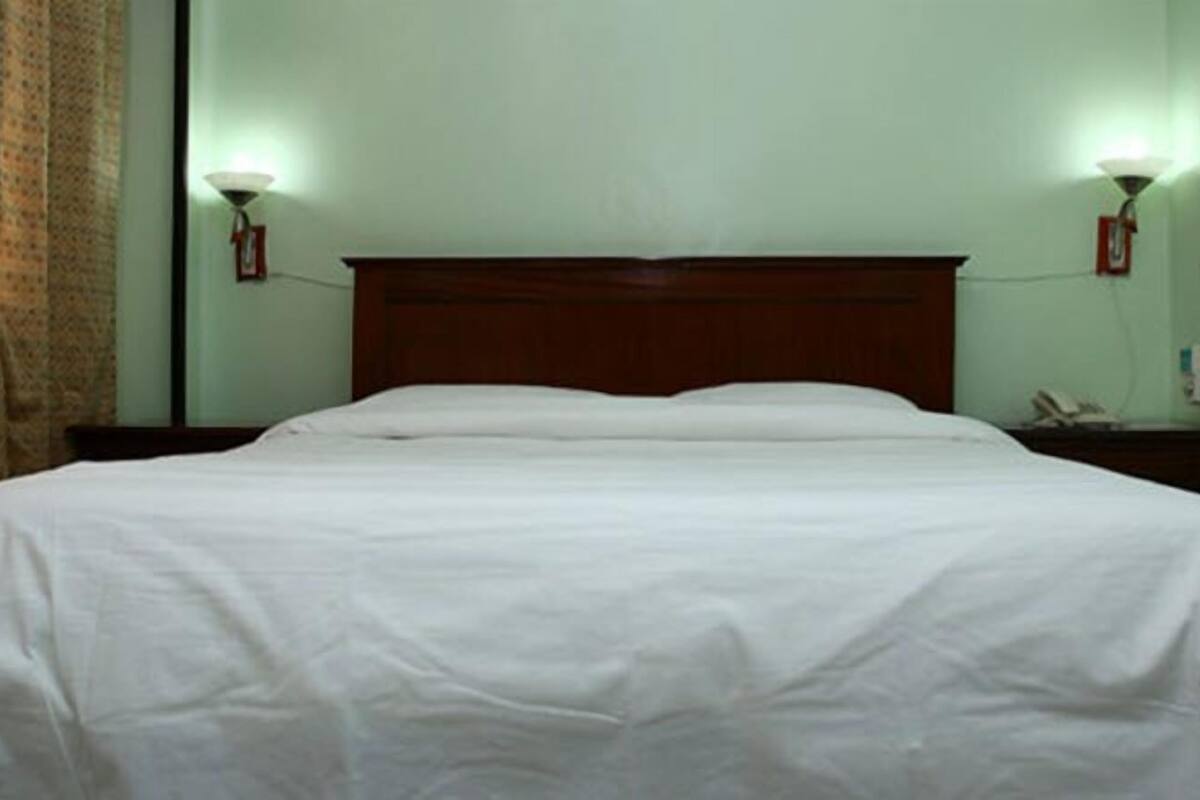 A neatly made bed in a room with a wooden headboard, two wall-mounted lamps, and a telephone on the nightstand.