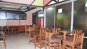 Un interior de restaurante con mesas y sillas de madera, una pantalla de televisión y un ventanal grande.