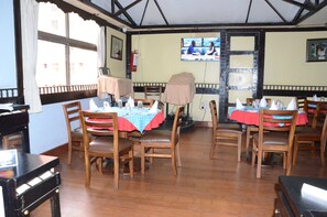 A restaurant with wooden tables and chairs, red and blue tablecloths, and a television screen on the wall.