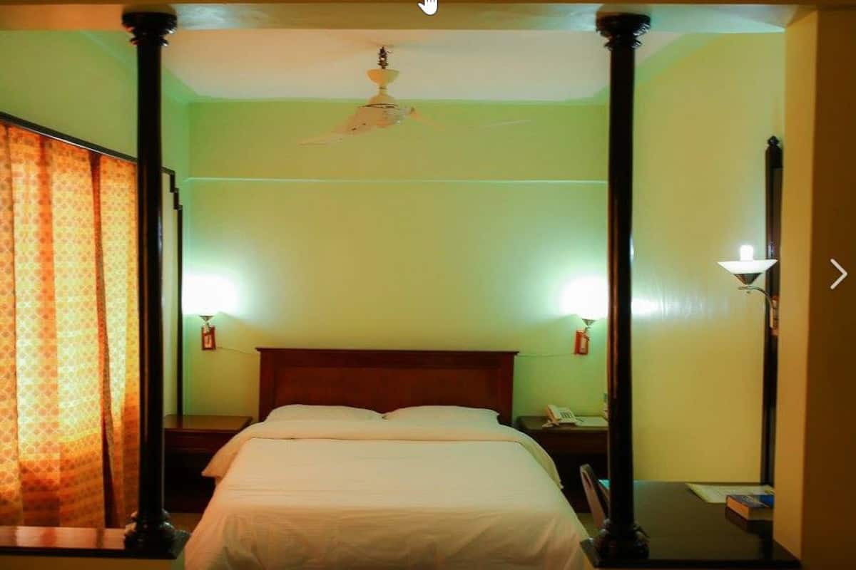A hotel room with a bed, nightstands, a telephone, and a ceiling fan.