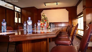 Un salón de conferencias con una larga mesa de madera, varias sillas, botellas de agua y un arreglo floral.