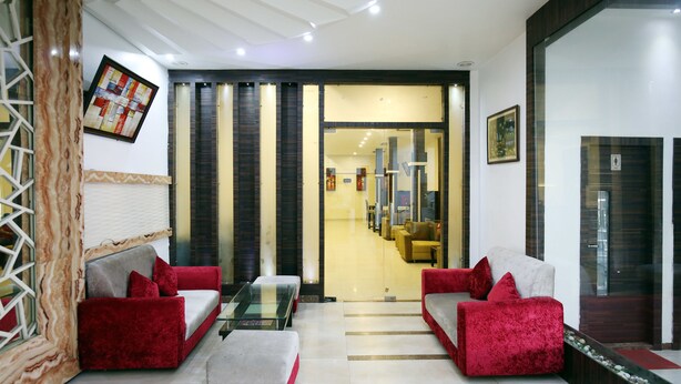 A modern lobby with red sofas, a glass coffee table, and a view into a dining area. - OYO 1673 Hotel MM Yellowuds (Amritsar)
