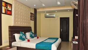 A neatly arranged bedroom with a large bed, a bedside table, a wardrobe, and an air conditioning unit on the wall. - OYO 1673 Hotel MM Yellowuds (Amritsar)