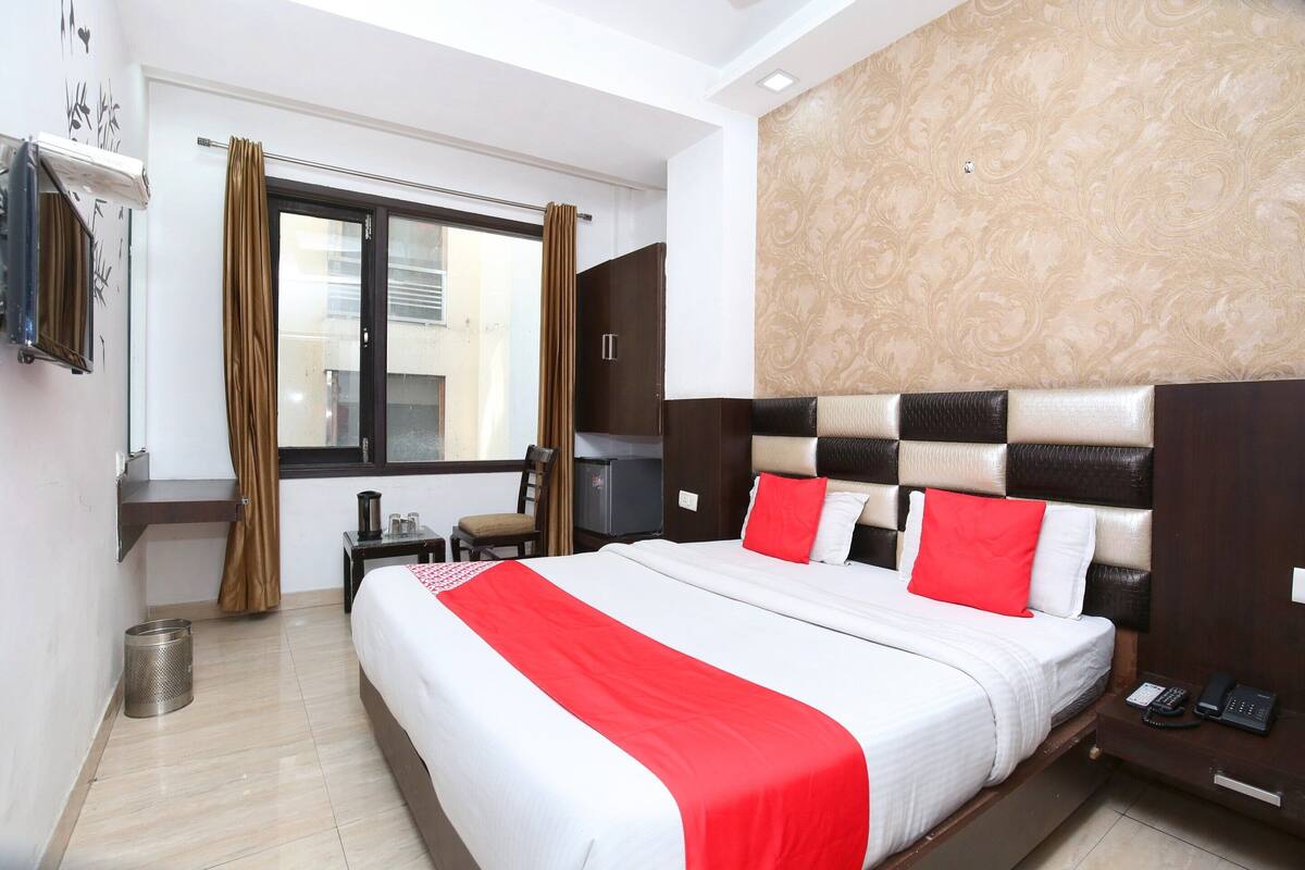 A hotel room with a large bed, a desk with a chair, a telephone, and a window with curtains.