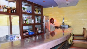 Een bar met flessenkasten vol drank, een kassa en barstoelen.