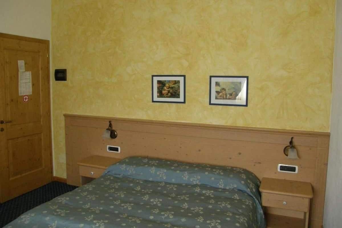 A hotel room with a wooden headboard, a bed with floral bedding, two bedside tables with lamps, and two framed pictures on the wall.