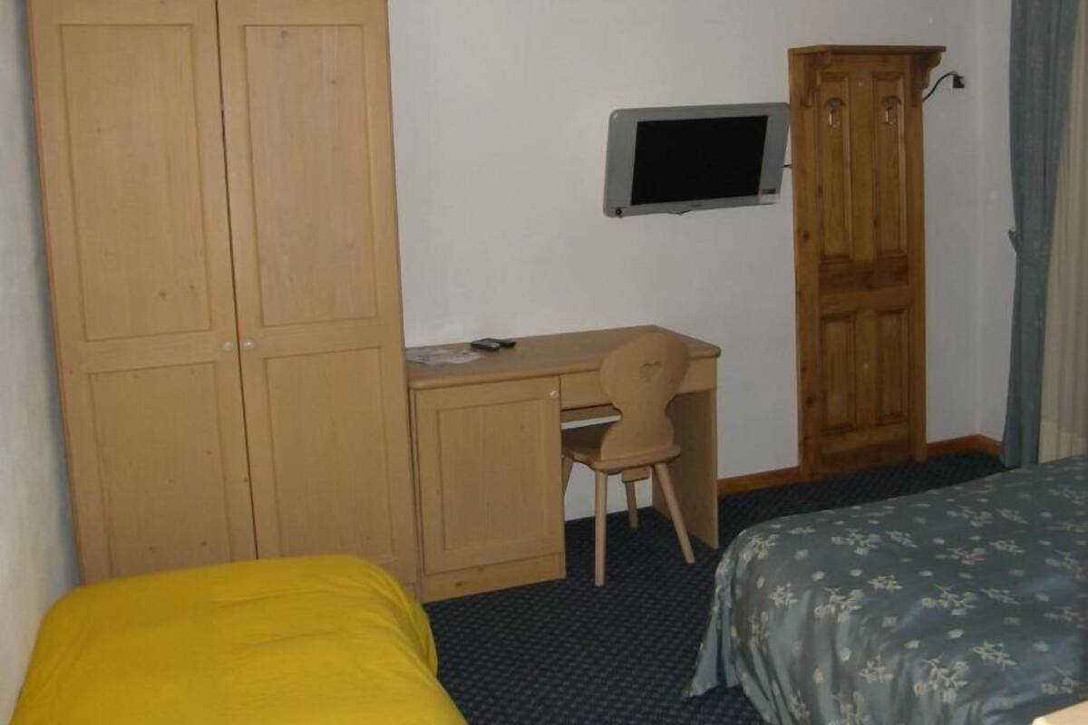 A room with a bed, a desk with a chair, a television, and a wardrobe.