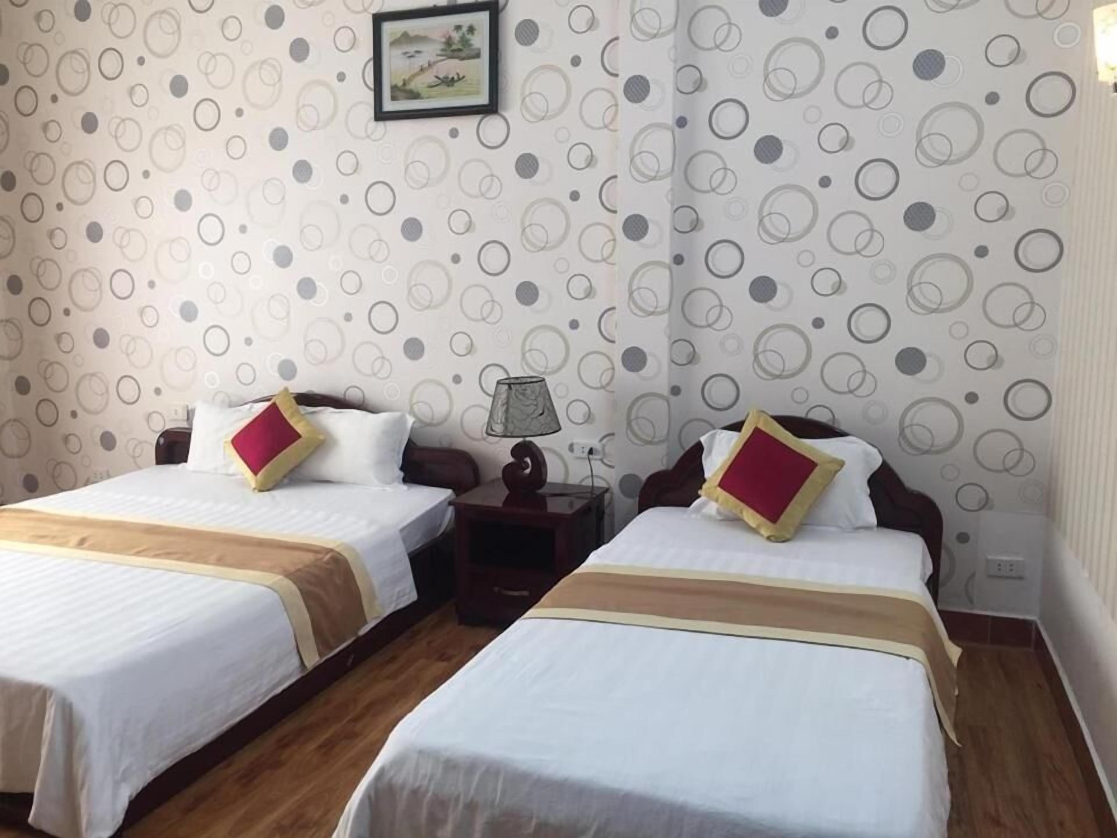 A hotel room with two beds, each with a red and yellow pillow, and a nightstand with a lamp between them.