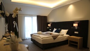 Een moderne hotelkamer met een groot bed, bedlampen, een houten nachtkastje en een vaas met witte bloemen.