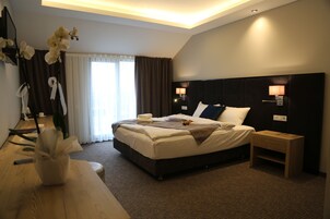 A modern hotel room with a large bed, bedside lamps, a wooden nightstand, and a vase with white flowers.